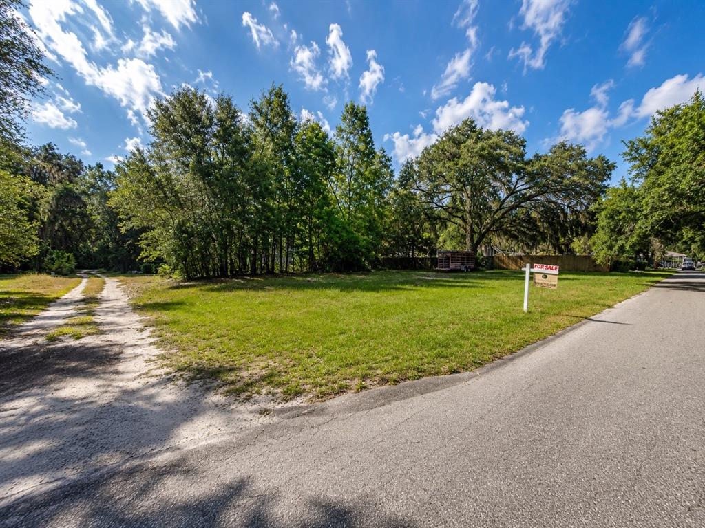 A vacant, grassy lot with trees and a for sale sign sits beside a paved road — GASKINS STREET, LEESBURG, FL