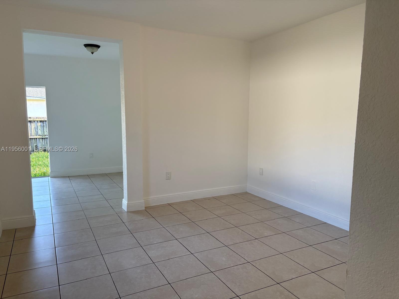 An empty room with beige tile flooring and white walls leads to a backyard view — 2916 NW 51st St, Miami FL 33142, MIAMI, FL