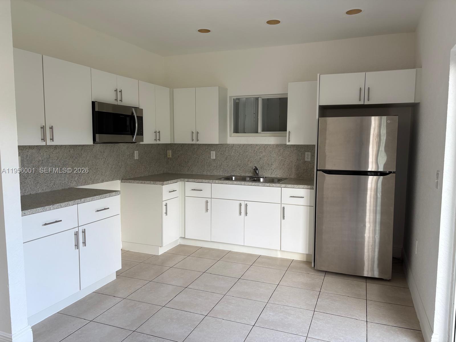 A kitchen features white cabinets, stainless steel appliances, granite countertops, and light-colored tile flooring — 2916 NW 51st St, Miami FL 33142, MIAMI, FL