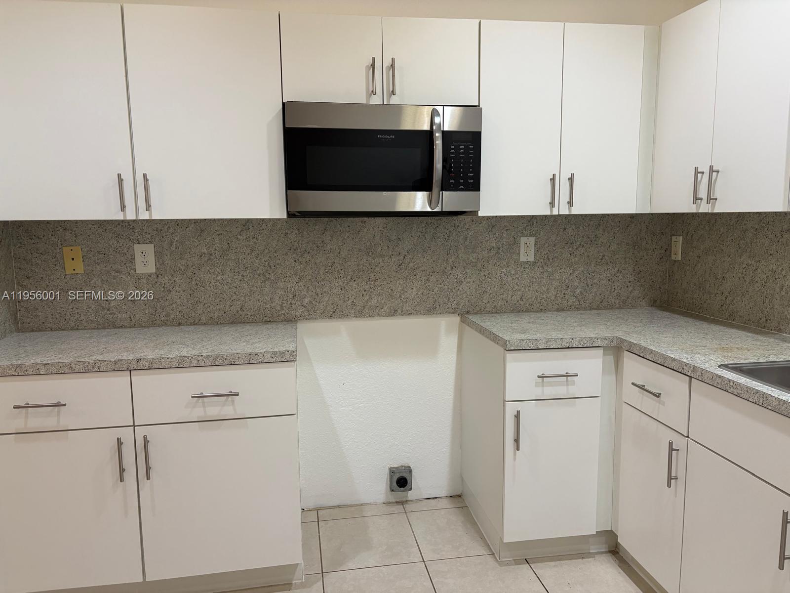 A kitchen features white cabinets, granite countertops, a stainless steel microwave, and a missing range — 2916 NW 51st St, Miami FL 33142, MIAMI, FL