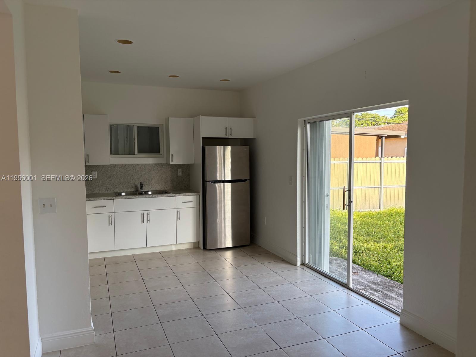 A kitchen with white cabinets, stainless steel appliances, and tile flooring opens to a backyard — 2916 NW 51st St, Miami FL 33142, MIAMI, FL