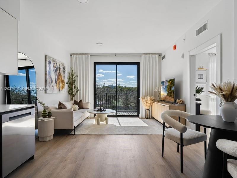 A modern living room features light wood floors, a sofa, a dining area, and balcony access — 2479 NE 192nd St # 207, Miami FL 33180, MIAMI, FL