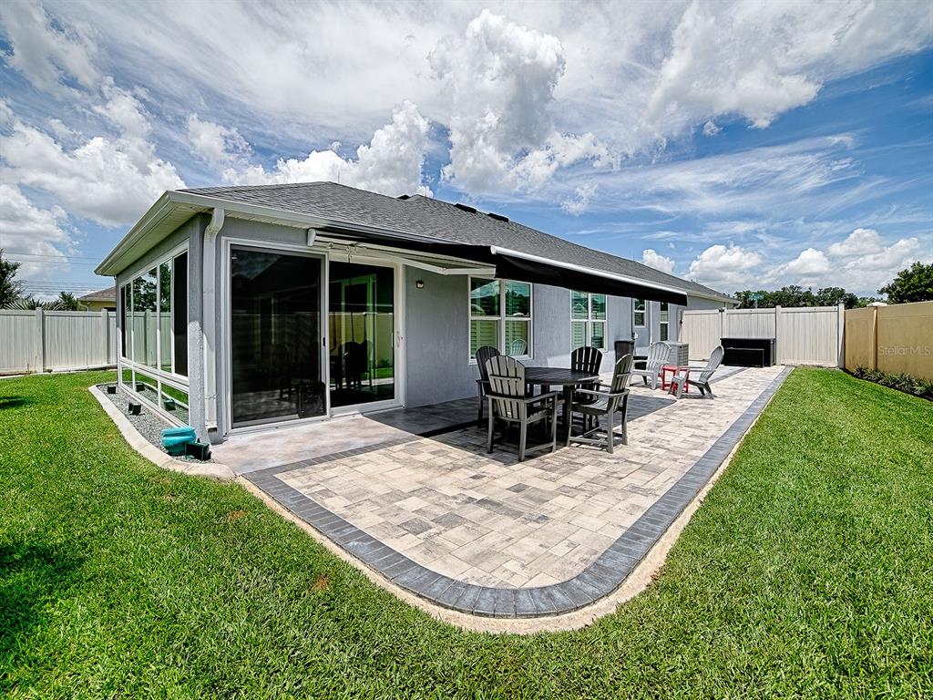 A backyard patio features a paved stone surface, outdoor dining furniture, and a retractable awning — 3394 RANDI ROAD, THE VILLAGES, FL