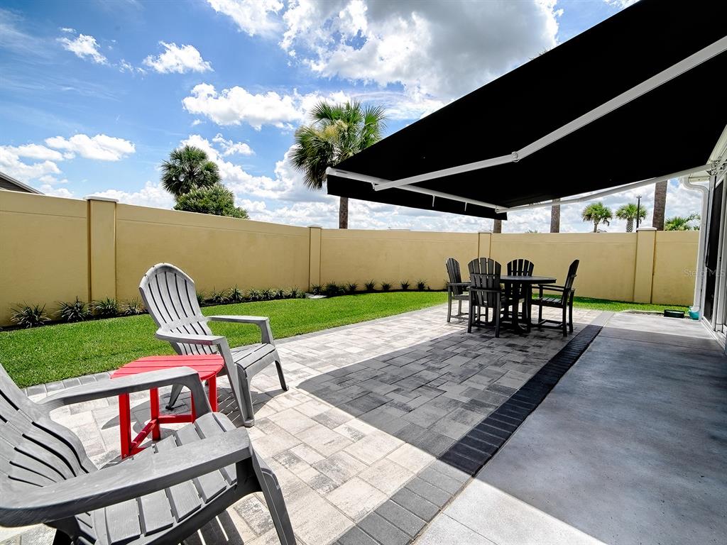 A patio with a retractable awning, dining set, and chairs overlooks a fenced backyard — 3394 RANDI ROAD, THE VILLAGES, FL