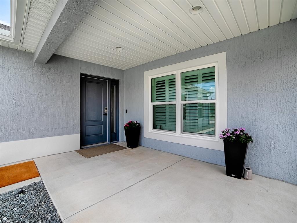 A covered concrete porch features a dark front door, a large window, and two planters — 3394 RANDI ROAD, THE VILLAGES, FL