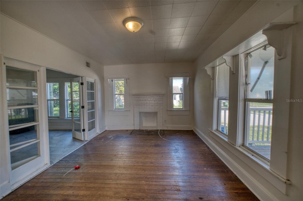 An empty room with hardwood floors, a white brick fireplace, and large windows — 128 AVENUE D SW, WINTER HAVEN, FL