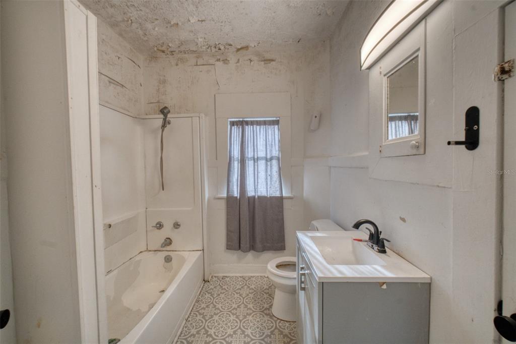 A bathroom with a tub-shower combo, a vanity, a toilet, and peeling ceiling paint — 128 AVENUE D SW, WINTER HAVEN, FL