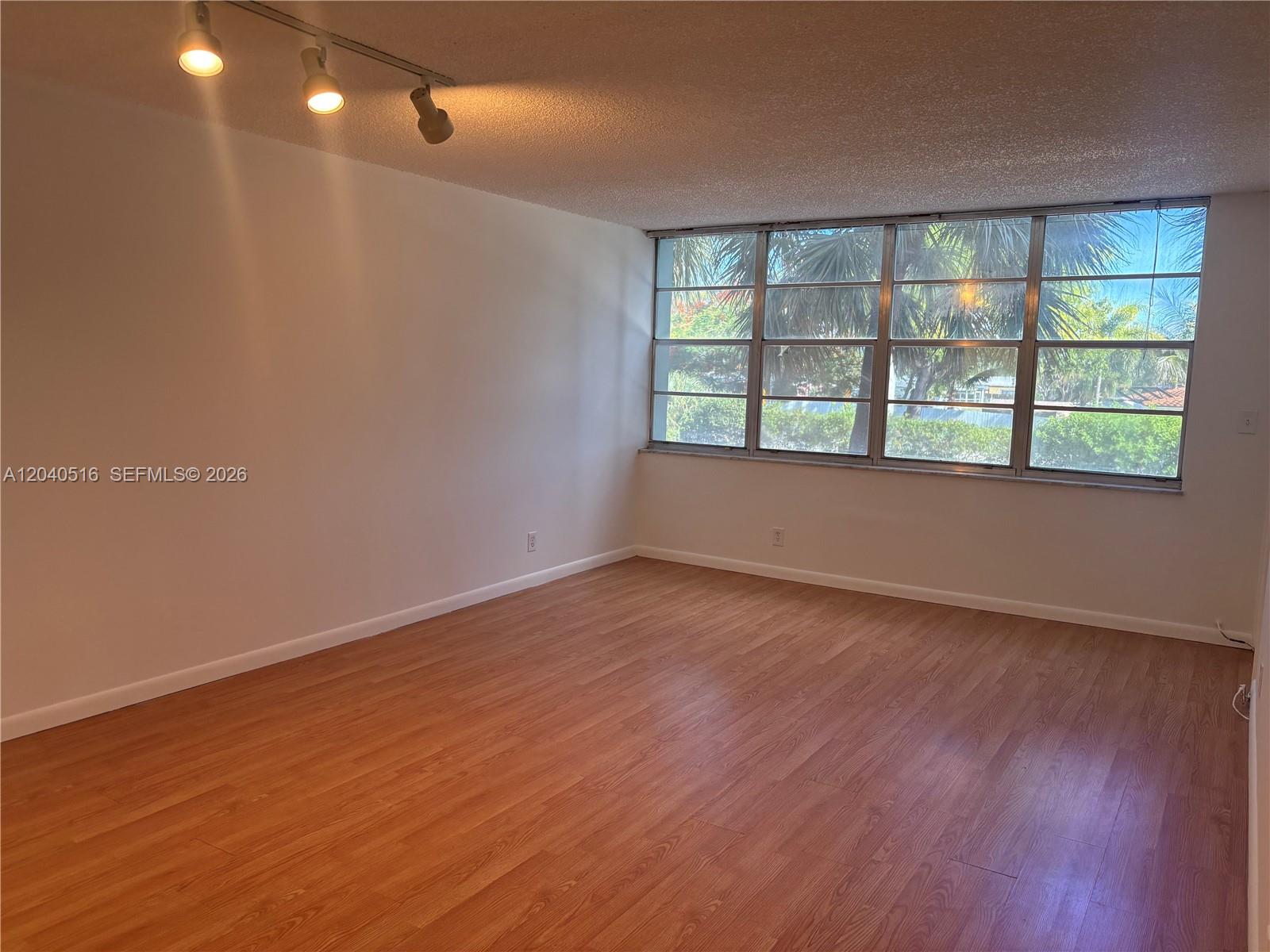 An empty room features wood-look flooring, white walls, a track light, and large windows — 2741 Taft St # 211, Hollywood FL 33020, HOLLYWOOD, FL