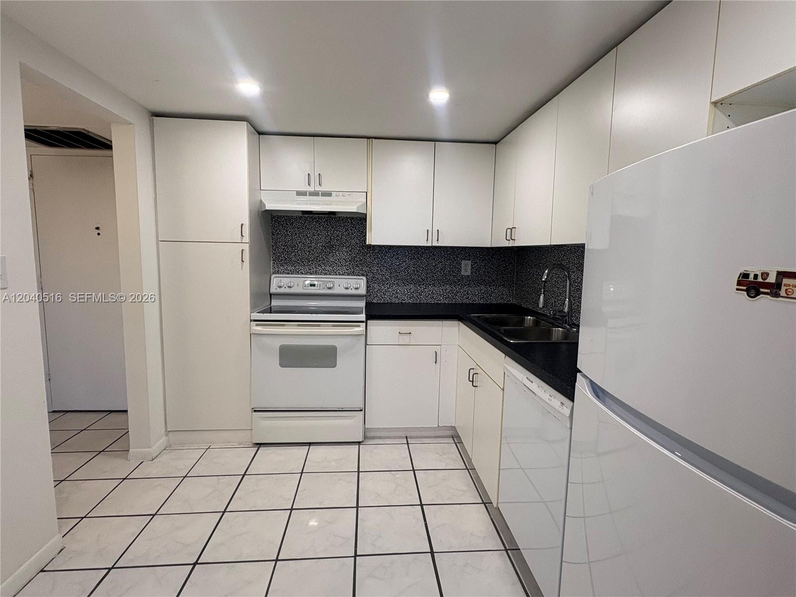 A kitchen features white cabinets, white appliances, black countertops, and white tiled flooring — 2741 Taft St # 211, Hollywood FL 33020, HOLLYWOOD, FL