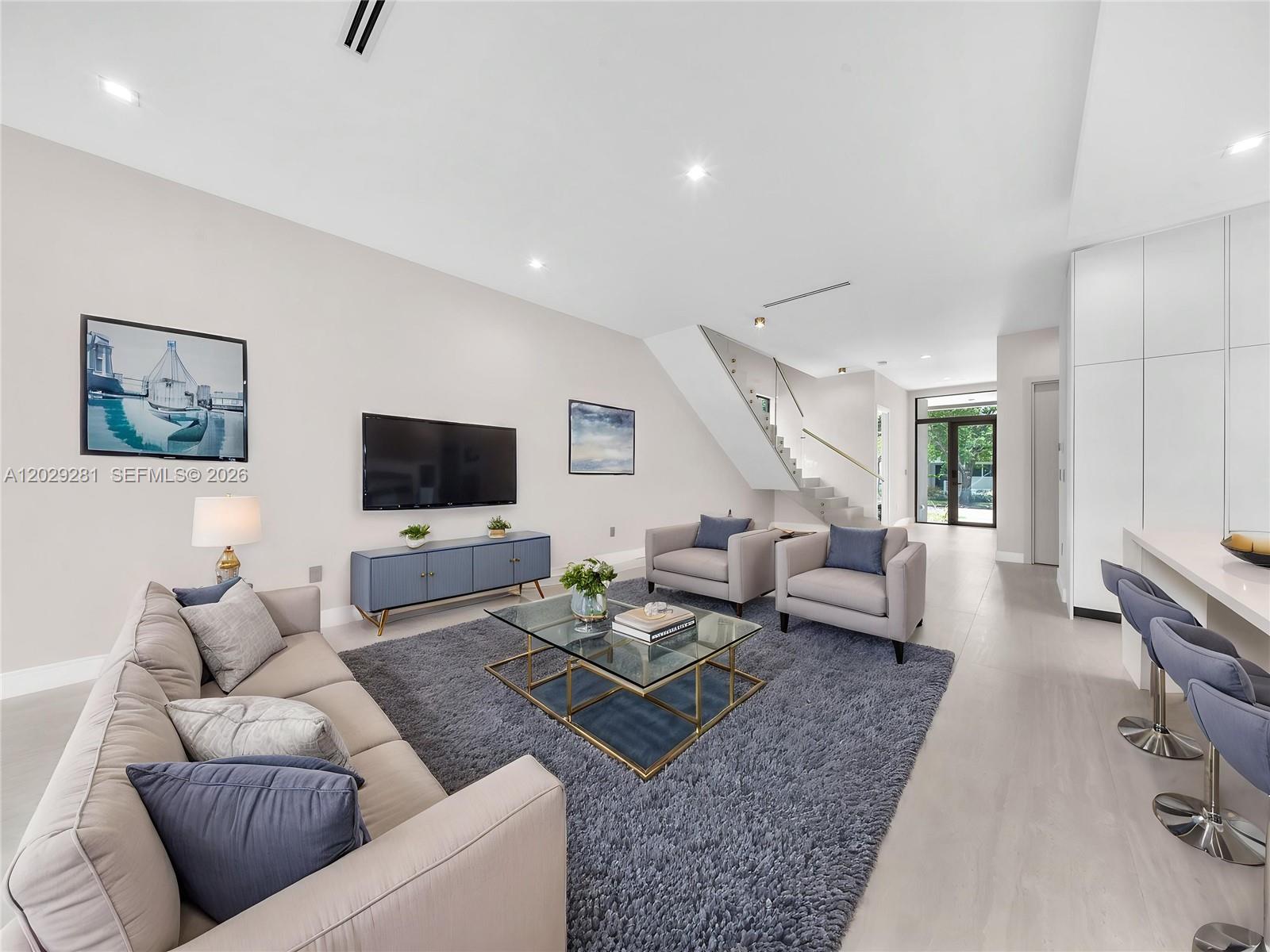 A modern living room features a grey sofa, two armchairs, a glass coffee table, and stairs — 1637 Monroe St, Hollywood FL 33020, HOLLYWOOD, FL