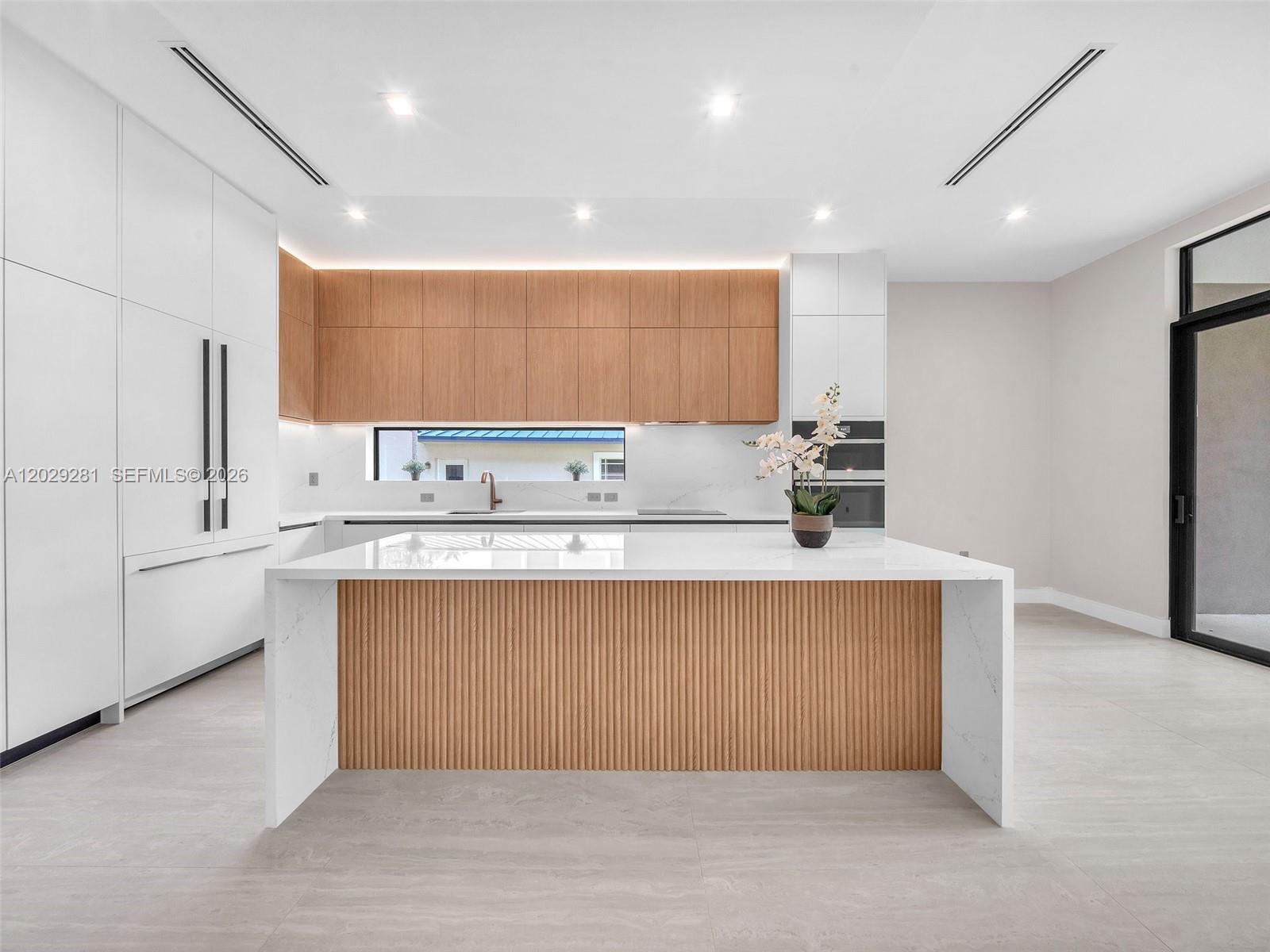 A modern kitchen features a white waterfall island with fluted wood paneling and cabinetry — 1637 Monroe St, Hollywood FL 33020, HOLLYWOOD, FL