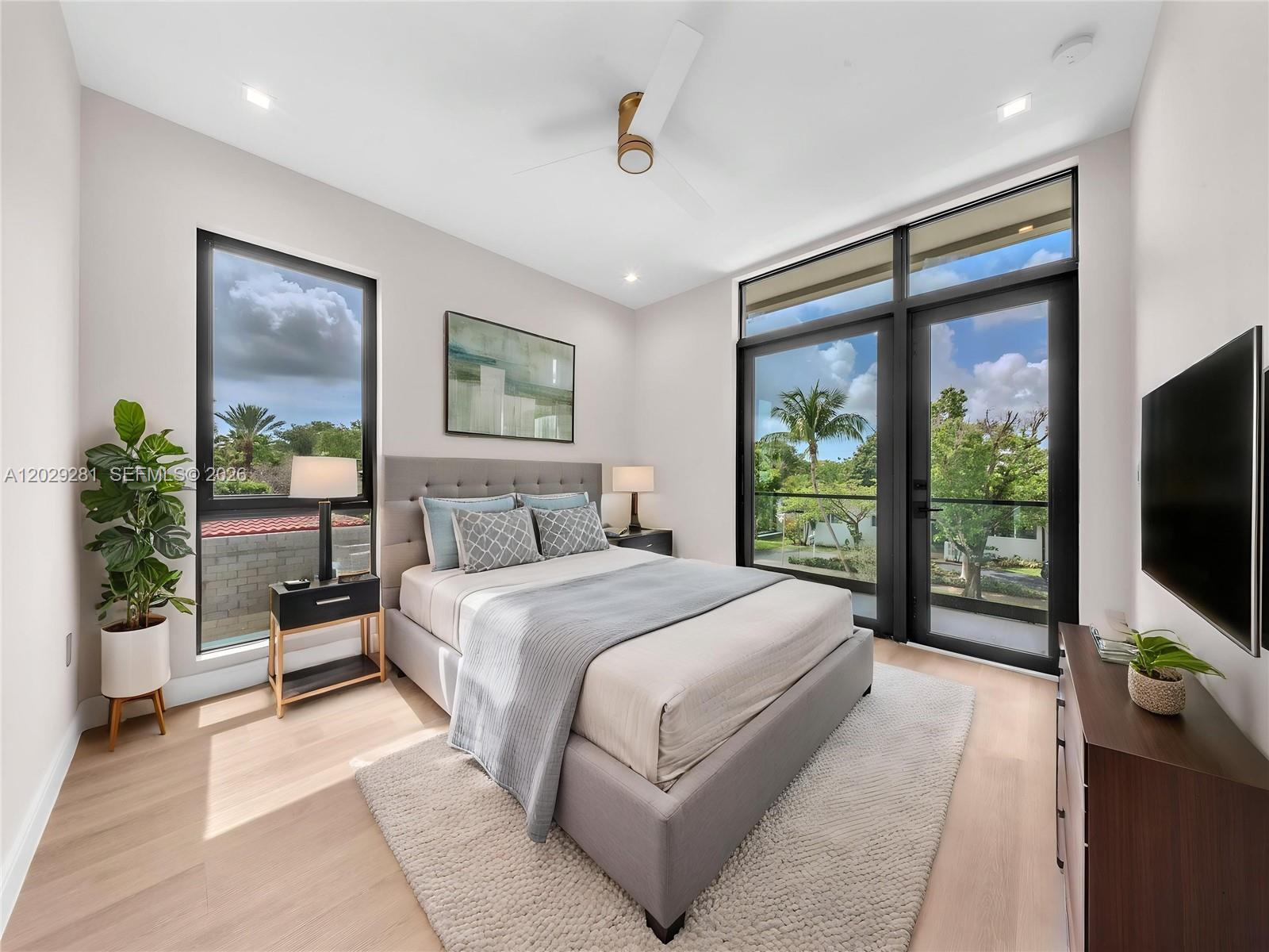 A modern bedroom features a gray upholstered bed, light wood floors, and large glass doors — 1637 Monroe St, Hollywood FL 33020, HOLLYWOOD, FL