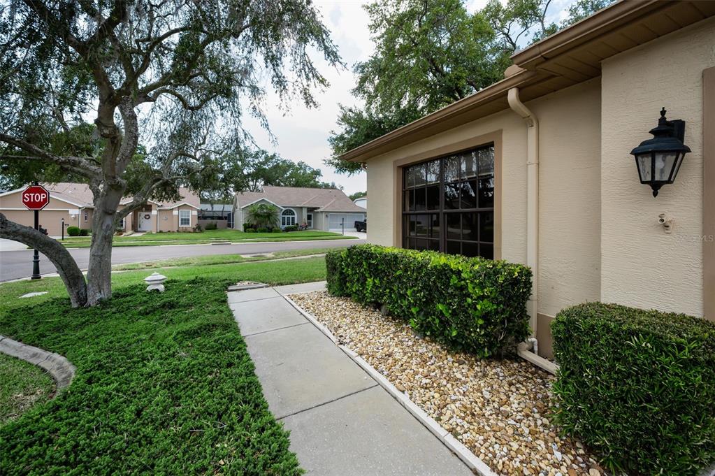 A tan house exterior features a window, a hedge, a walkway, and a nearby street — 9307 PALM HAVEN COURT, NEW PORT RICHEY, FL