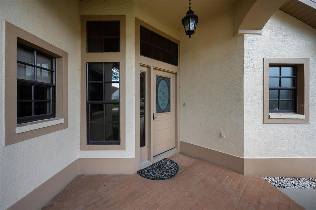 A beige front door with a decorative window sits on a tiled porch entrance — 9307 PALM HAVEN COURT, NEW PORT RICHEY, FL