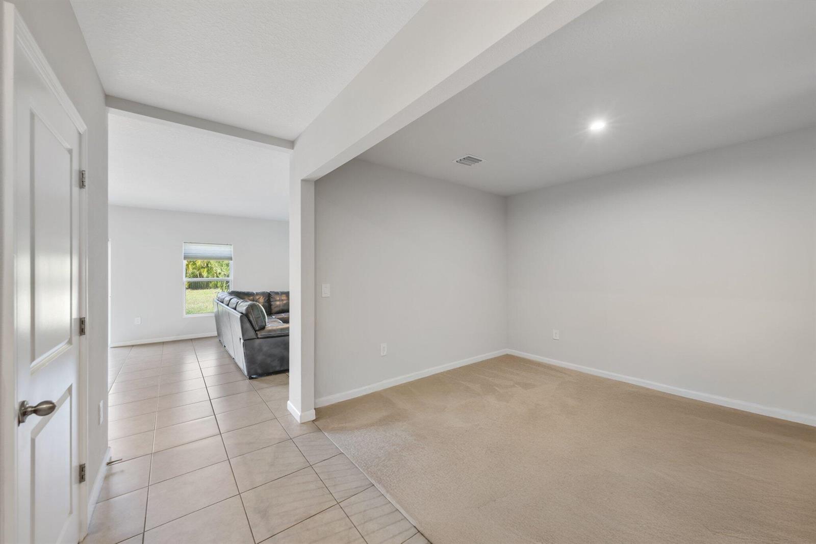 A carpeted room with light walls connects to a tiled living area with a sofa — 514 Raspberry Road, Fort Pierce FL 34981, FORT PIERCE, FL