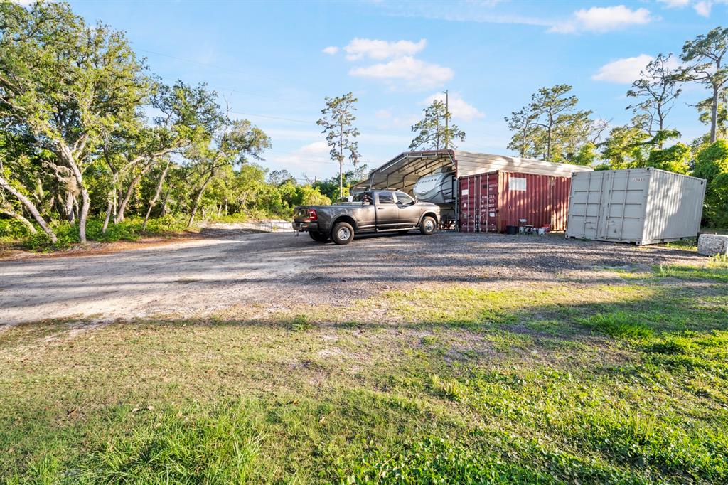 A pickup truck is parked under a metal carport next to two shipping containers outdoors — 1000 SR 415, DELTONA, FL