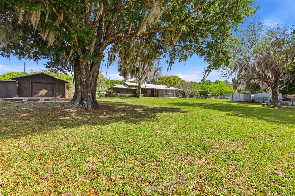 A large grassy yard features a detached garage, a house with a screened porch, and trees — 125 TWIN LAKE GROVE DRIVE, INTERLACHEN, FL