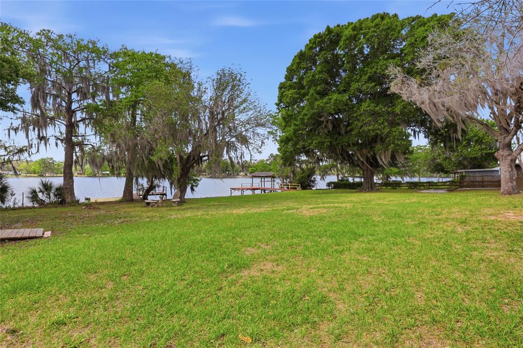 A grassy backyard leads to a lake with a wooden dock and large trees — 125 TWIN LAKE GROVE DRIVE, INTERLACHEN, FL