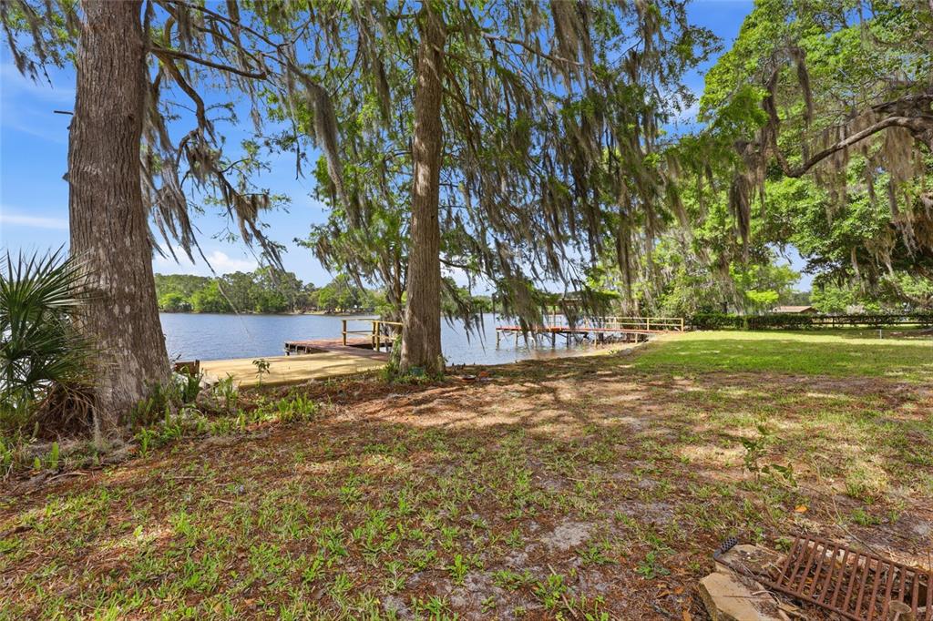 A wooden dock extends into a lake from a grassy yard shaded by mossy trees — 125 TWIN LAKE GROVE DRIVE, INTERLACHEN, FL