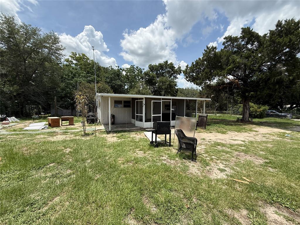 A small, single-story home with a screened-in porch sits on a grassy, partially wooded lot — 10360 SE 131ST LANE, OCKLAWAHA, FL
