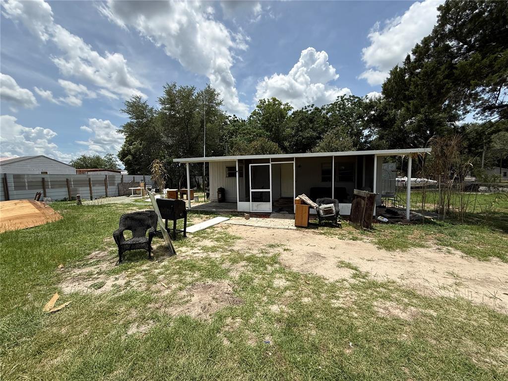 A single-story house with a screened-in porch sits on a grassy lot with scattered furniture — 10360 SE 131ST LANE, OCKLAWAHA, FL