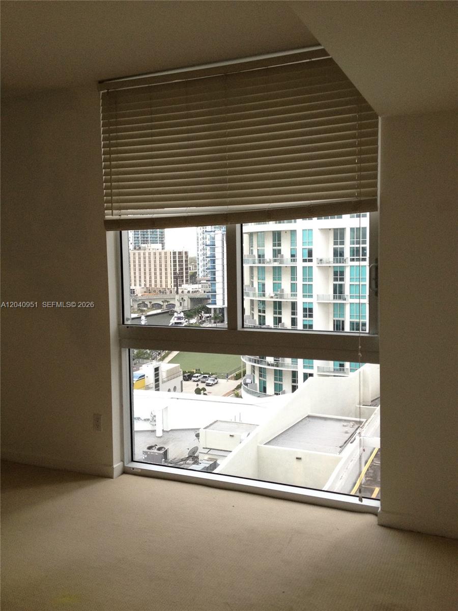 A carpeted room features a large window with blinds overlooking a city skyline and canal — 325 S Biscayne Blvd # 1414, Miami FL 33131, MIAMI, FL