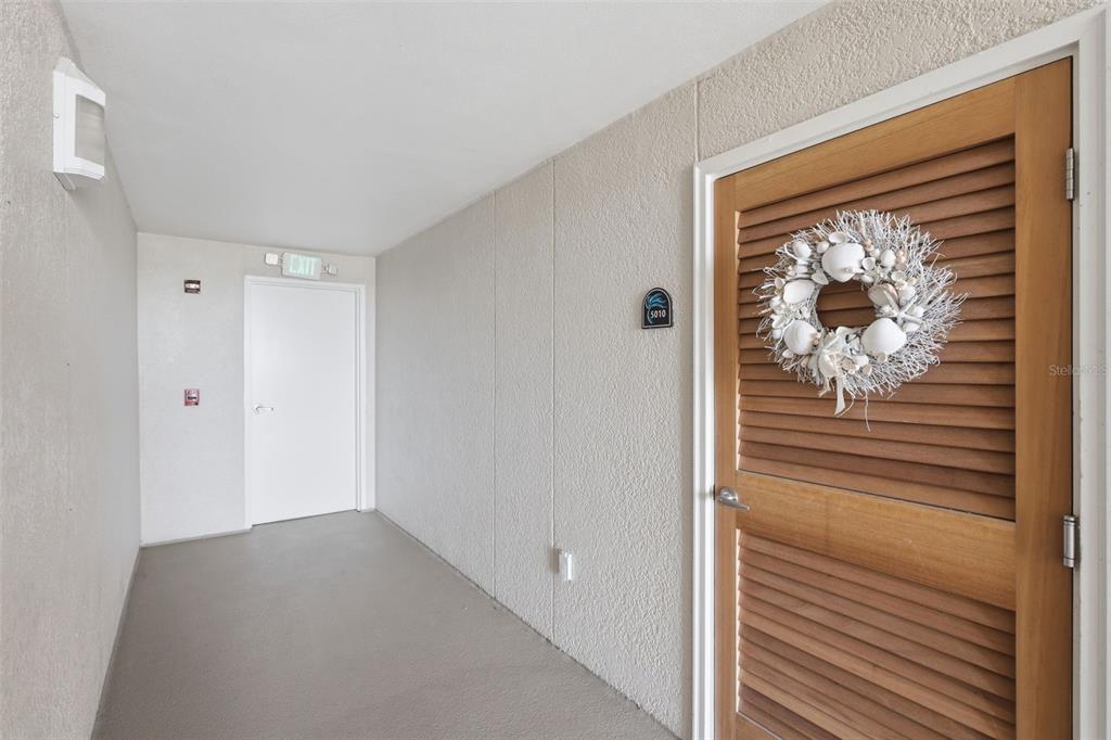 A hallway features a wooden louvered door with a seashell wreath and a white exit door — 4495 S ATLANTIC AVENUE UNIT 501, PONCE INLET, FL