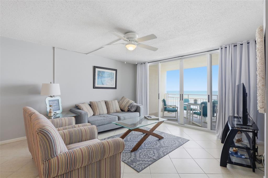 A living room features a striped armchair, a gray sofa, a glass coffee table, and balcony access — 4495 S ATLANTIC AVENUE UNIT 501, PONCE INLET, FL