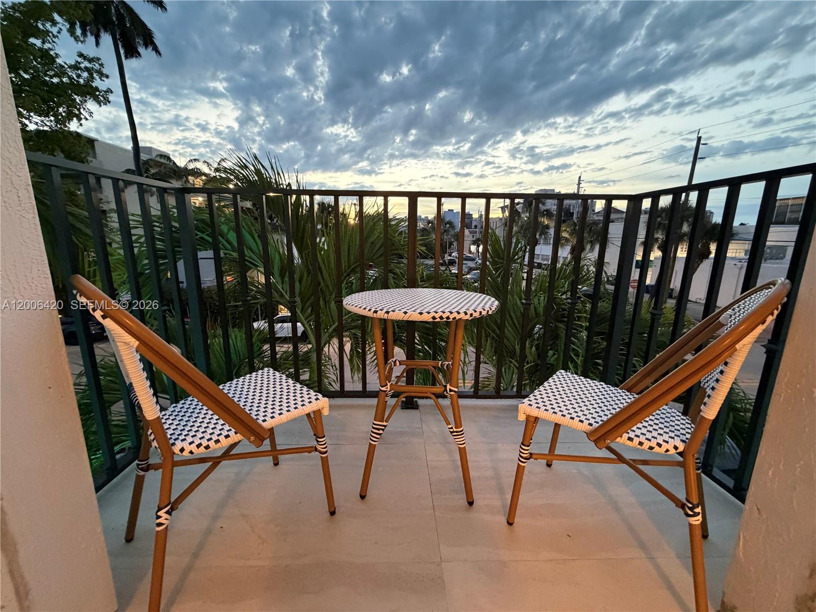 A balcony features a small bistro table and two chairs overlooking a street at sunset — 1619 Jefferson Ave # 16, Miami Beach FL 33139, MIAMI BEACH, FL