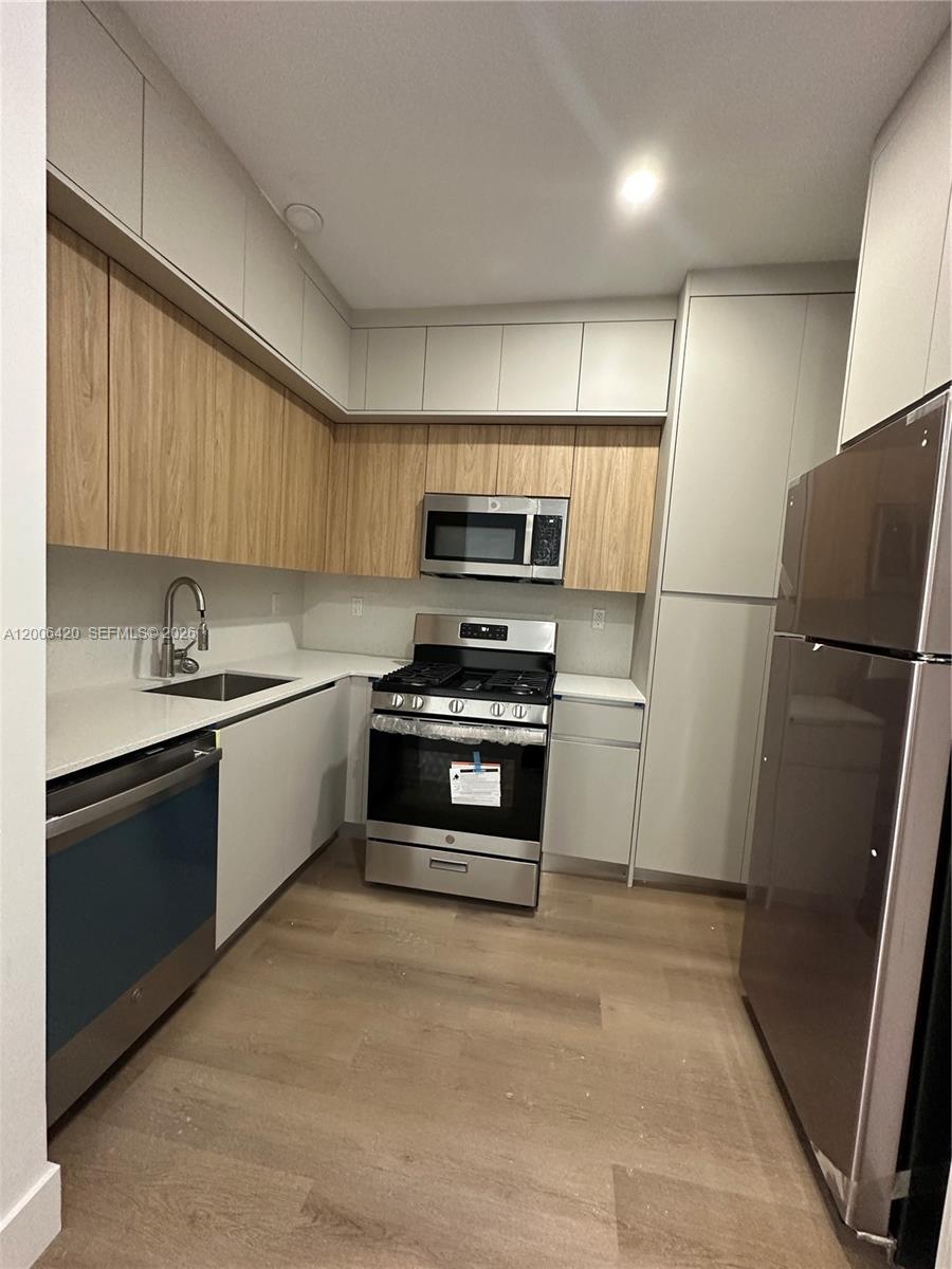A modern kitchen features light wood cabinets, white countertops, and stainless steel appliances — 1619 Jefferson Ave # 16, Miami Beach FL 33139, MIAMI BEACH, FL