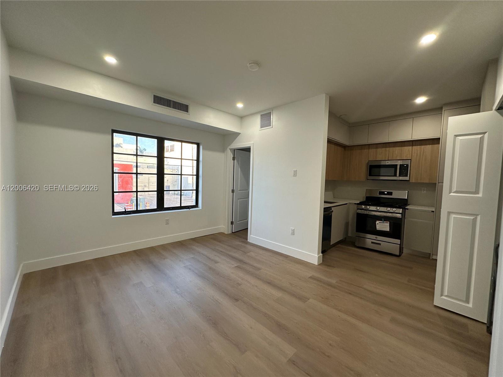 An open-concept room features light wood flooring, a window, and a kitchen with stainless appliances — 1619 Jefferson Ave # 16, Miami Beach FL 33139, MIAMI BEACH, FL