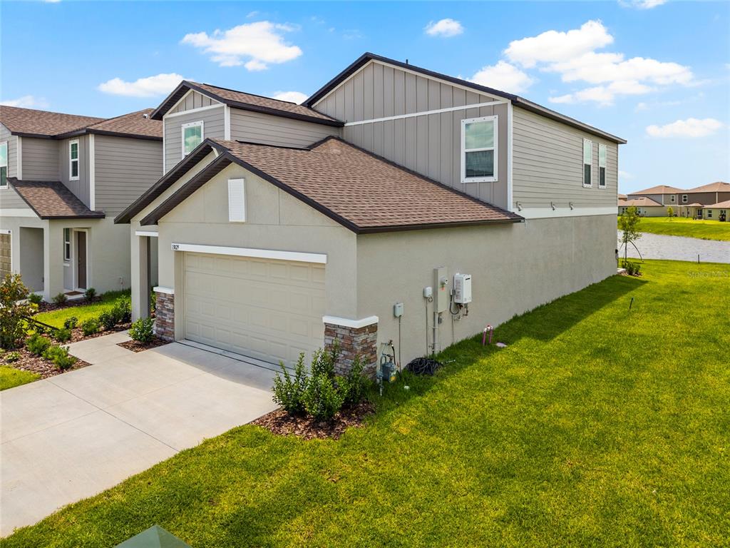 A two-story suburban house with a beige stucco exterior, stone accents, and a concrete driveway — 13029 EMPRESS JEWEL TRAIL, PARRISH, FL