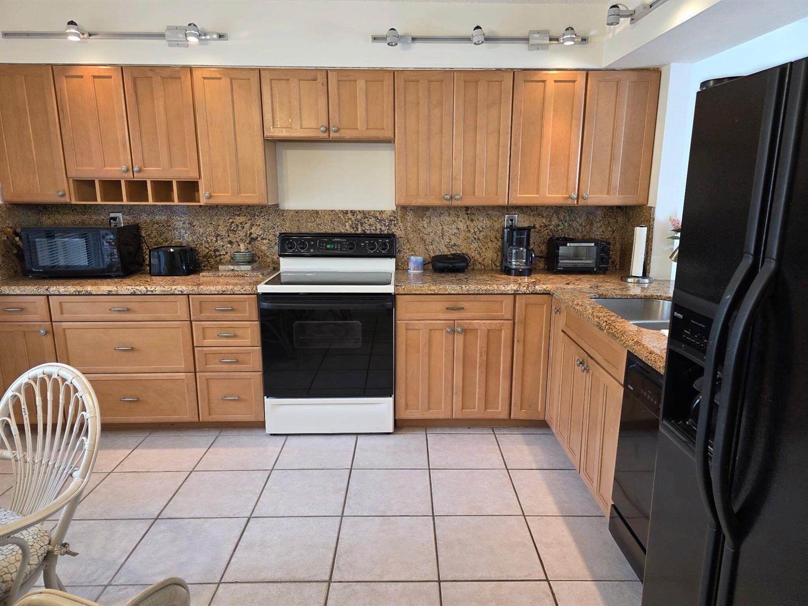 A kitchen with light wood cabinets, granite countertops, black appliances, and light-colored tile flooring — 11142 Green Lake Drive # 202, Boynton Beach FL 33437, BOYNTON BEACH, FL