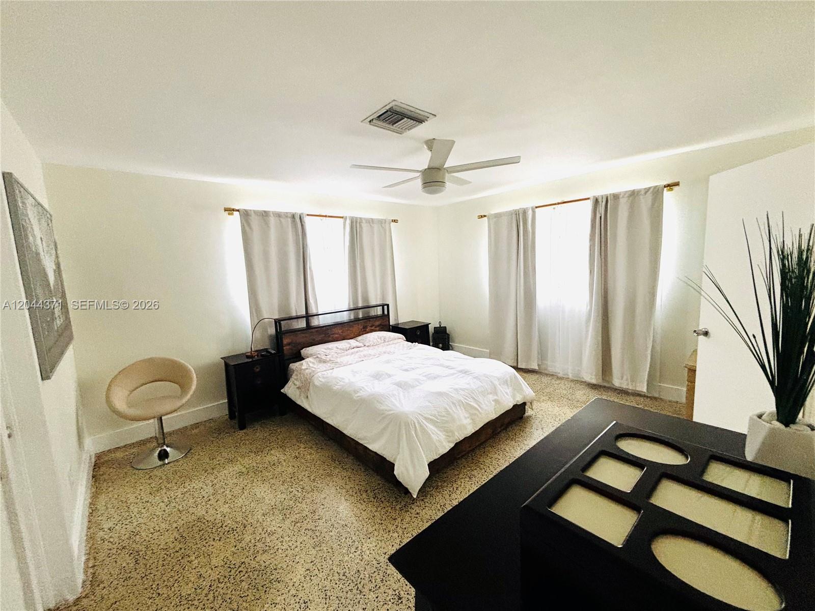A bedroom features a bed, two windows with curtains, a ceiling fan, and terrazzo flooring — NORTH MIAMI BEACH, FL