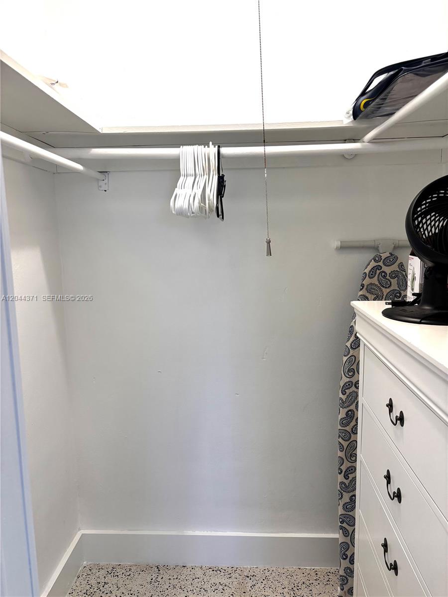 A white closet features a hanging rod, a shelf, and a dresser with an ironing board — NORTH MIAMI BEACH, FL