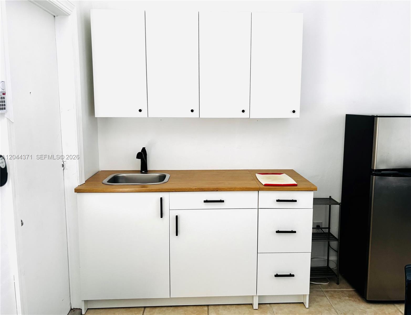 A kitchenette features white cabinets, a wood countertop, a stainless steel sink, and a refrigerator — NORTH MIAMI BEACH, FL