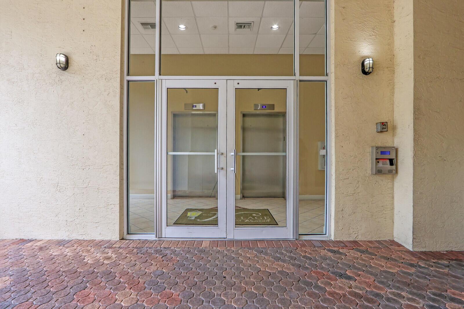 A ground-level exterior view of a glass double-door entrance featuring two elevators inside — 1155 Main Street # 216, Jupiter FL 33458, JUPITER, FL