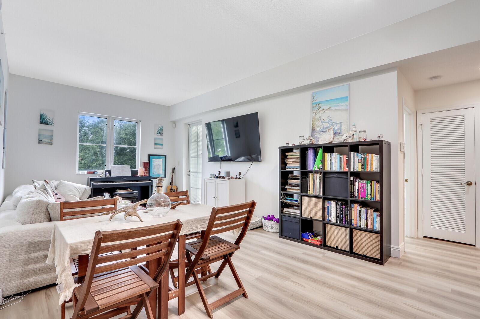 A living and dining area features a wooden table, chairs, a bookshelf, and a television — 1155 Main Street # 216, Jupiter FL 33458, JUPITER, FL