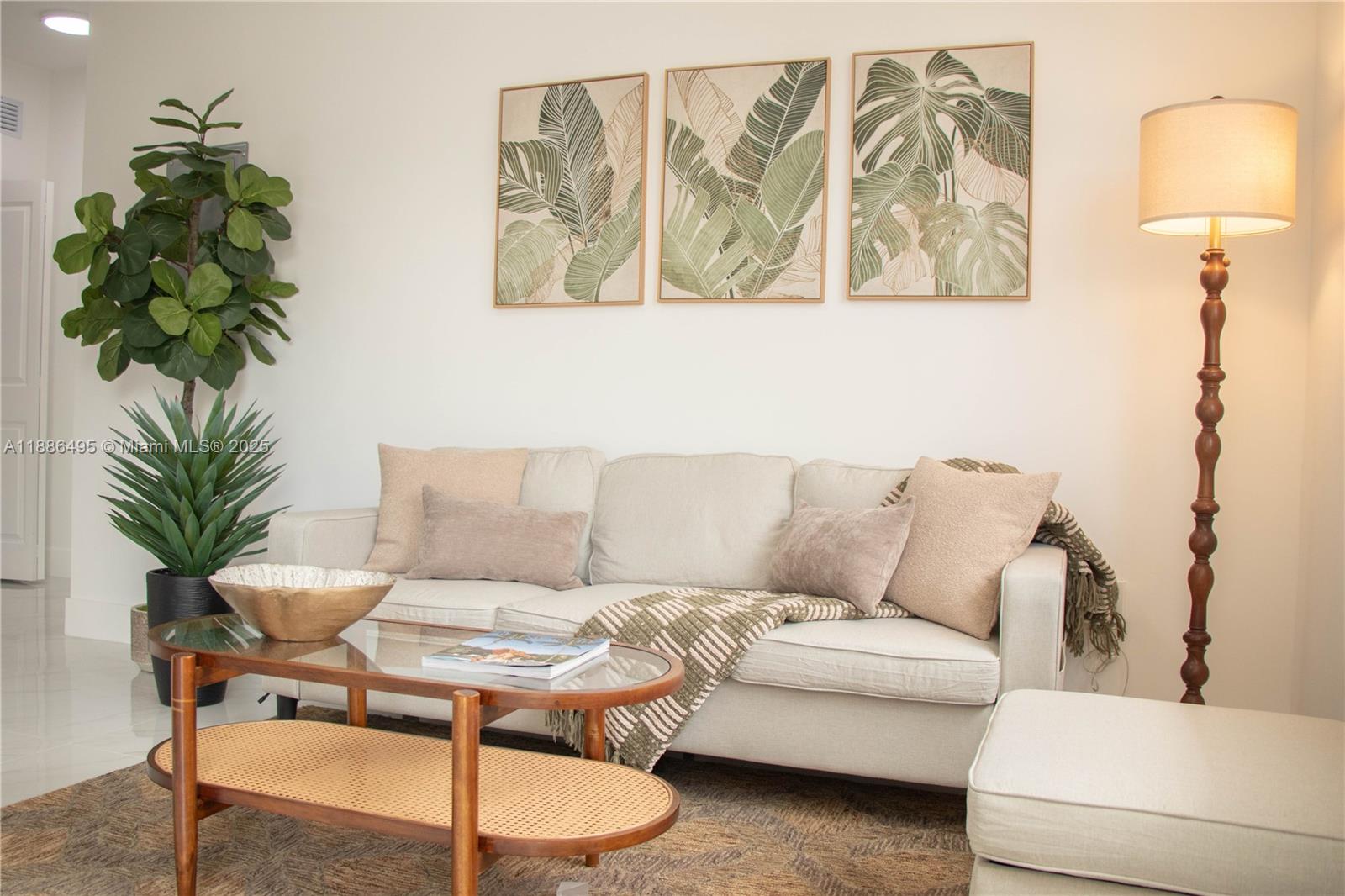 A living room features a beige sofa, a glass coffee table, and botanical wall art — 1453 W 29th St # 307, Hialeah FL 33012, HIALEAH, FL