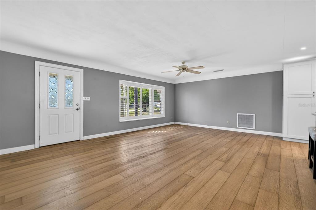 A living room with gray walls, light wood flooring, a ceiling fan, and a front door — 1276 37TH AVENUE NE, ST PETERSBURG, FL