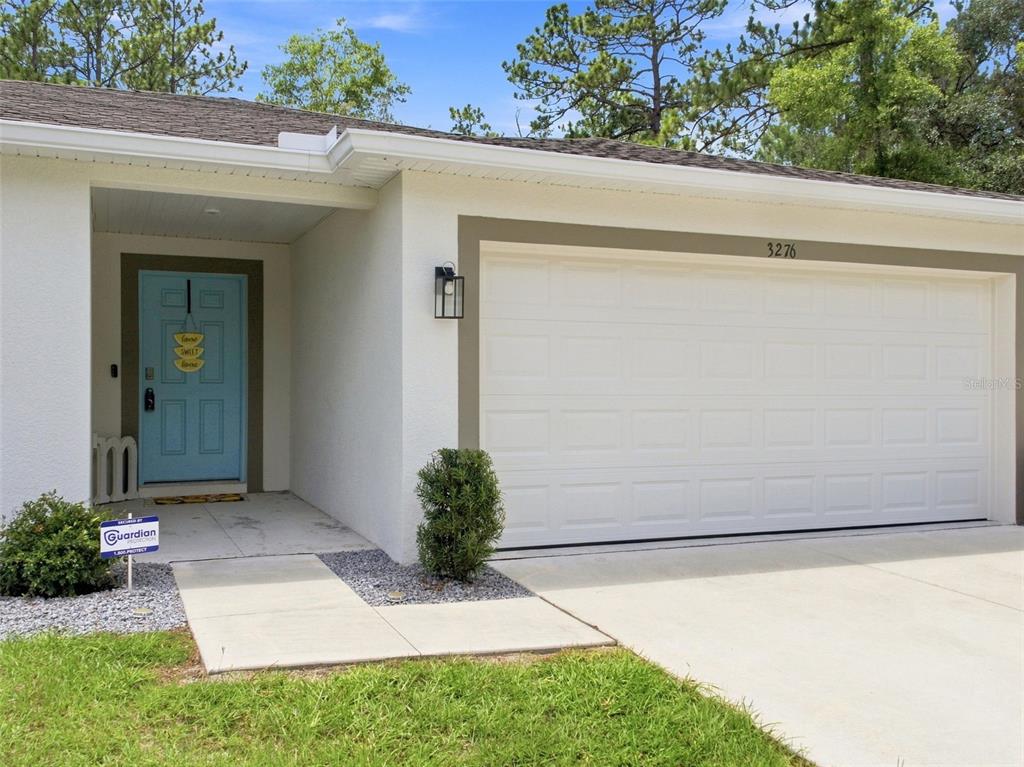The exterior of a house features a white garage door, a light blue front door, and landscaping — 3276 W CAMILO DRIVE, DUNNELLON, FL