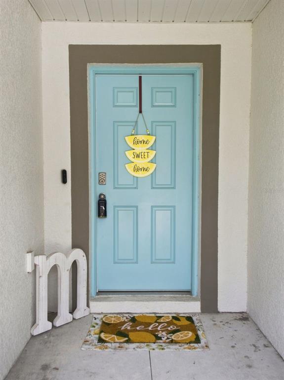 A light blue front door with a lemon-themed sign and welcome mat sits under a porch — 3276 W CAMILO DRIVE, DUNNELLON, FL