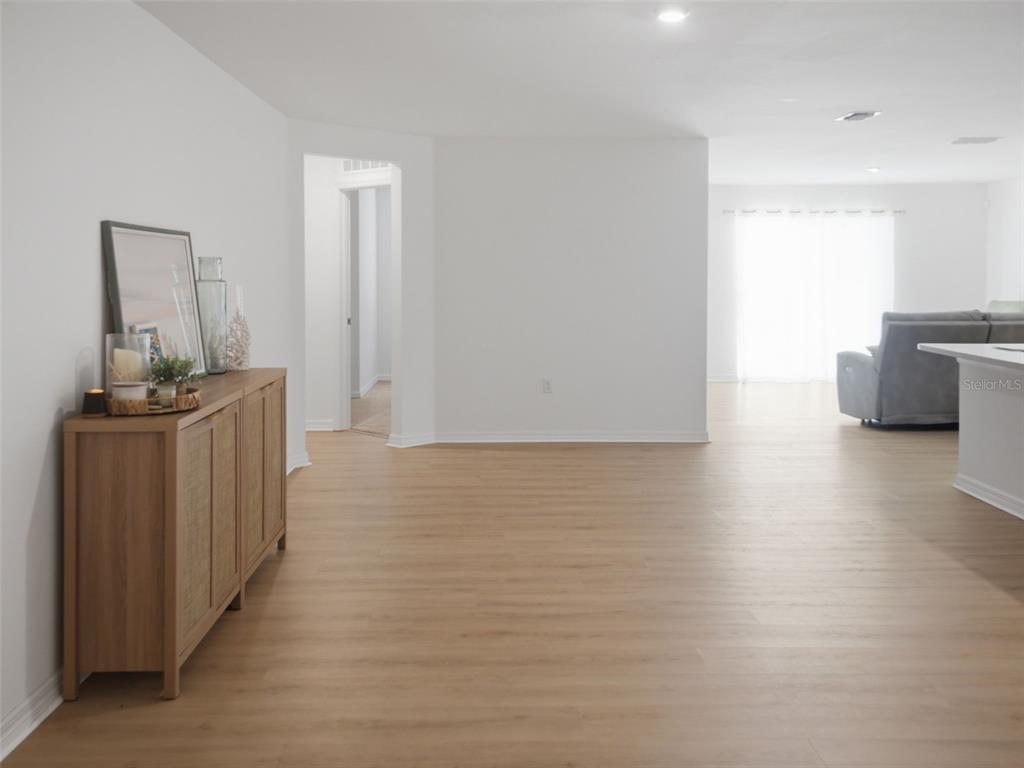 A bright, open-concept living area features light wood-look flooring, white walls, and a wooden sideboard — 3276 W CAMILO DRIVE, DUNNELLON, FL