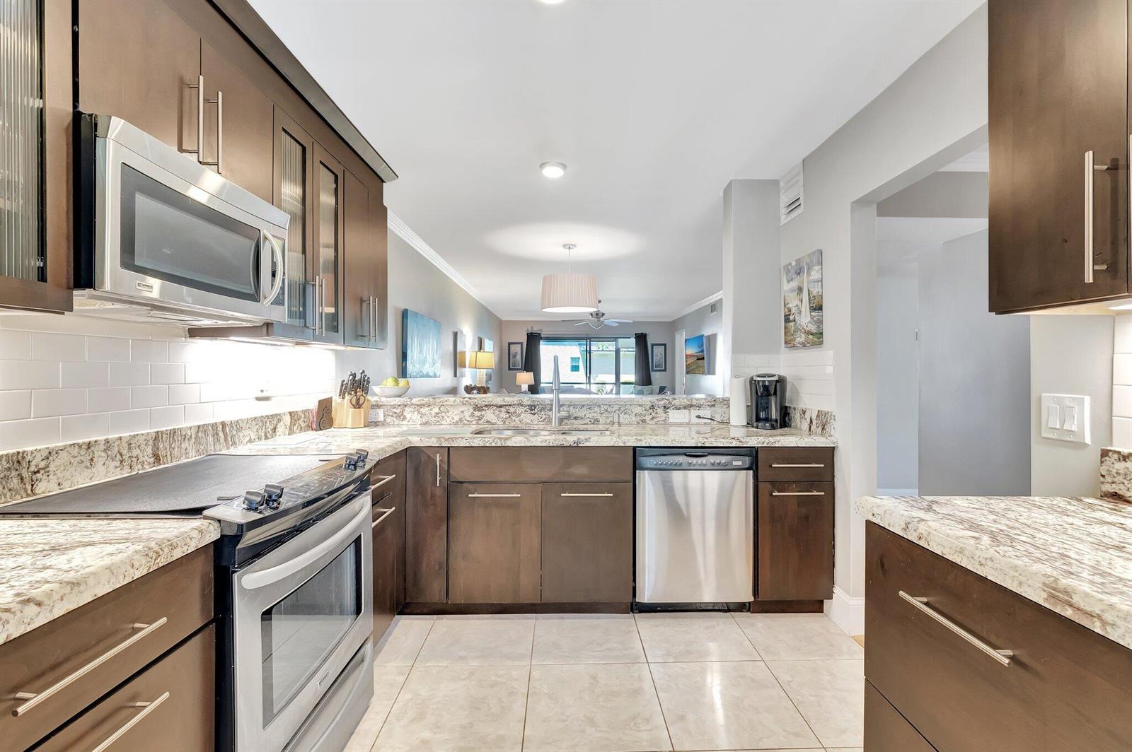 A kitchen with dark wood cabinets, granite countertops, stainless steel appliances, and white tile flooring — 701 Avenue L, Delray Beach FL 33483, DELRAY BEACH, FL