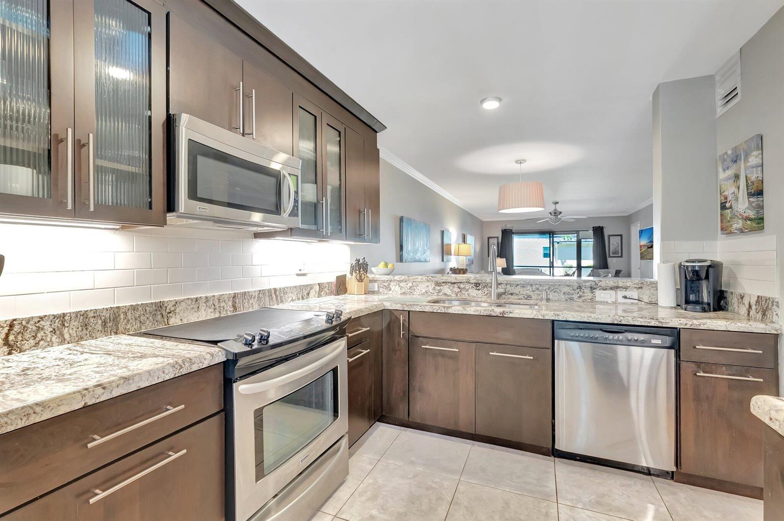 A kitchen features dark wood cabinets, stainless steel appliances, granite countertops, and a white backsplash — 701 Avenue L, Delray Beach FL 33483, DELRAY BEACH, FL