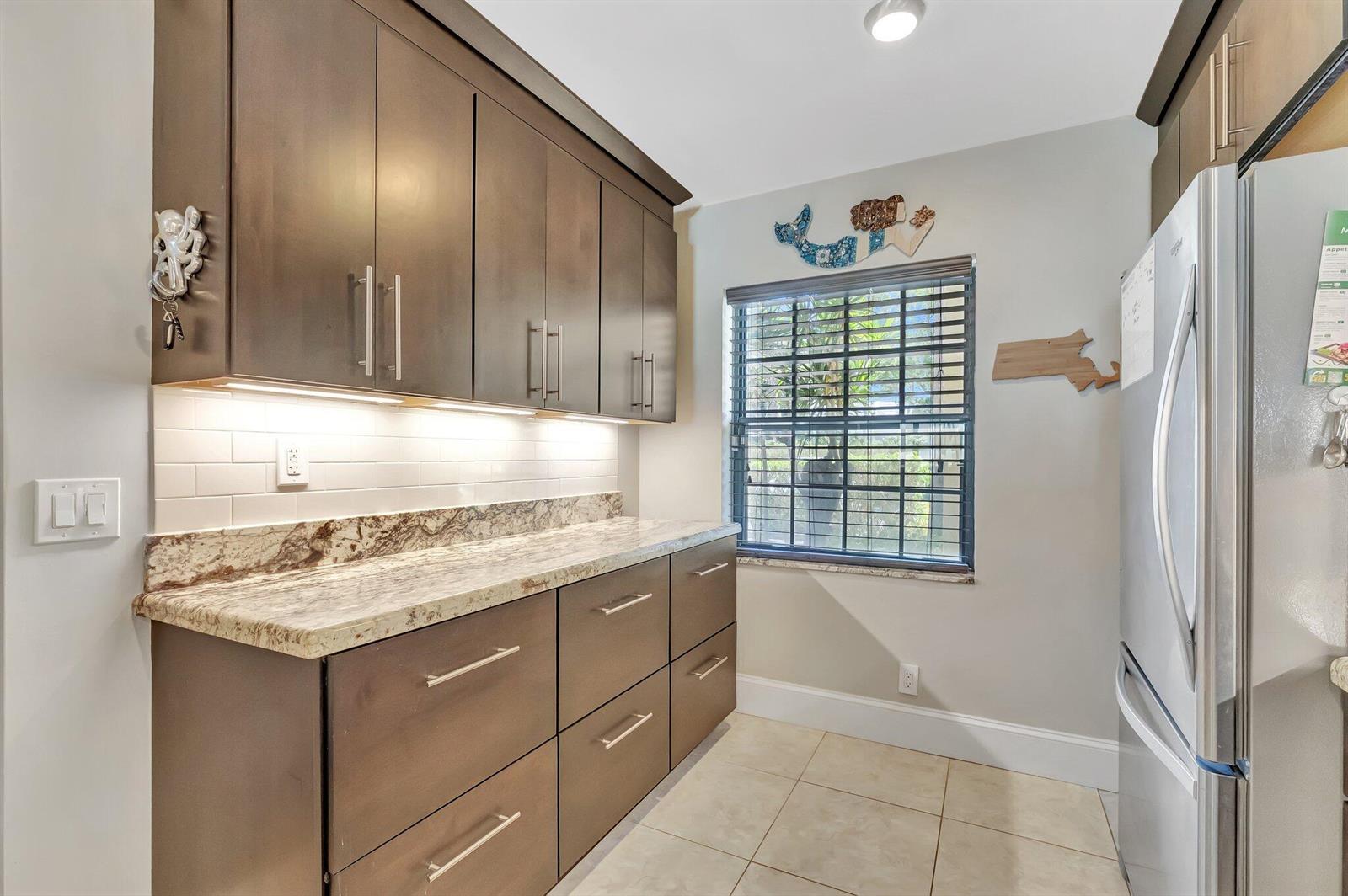 A kitchen area features dark wood cabinets, granite countertops, a white subway tile backsplash, and stainless-steel appliances — 701 Avenue L, Delray Beach FL 33483, DELRAY BEACH, FL
