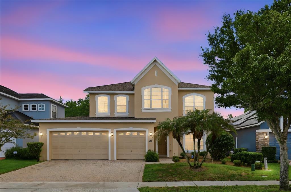 A two-story suburban house with a tan stucco exterior, a two-car garage, and a palm tree — 16368 TUDOR GROVE DRIVE, ORLANDO, FL
