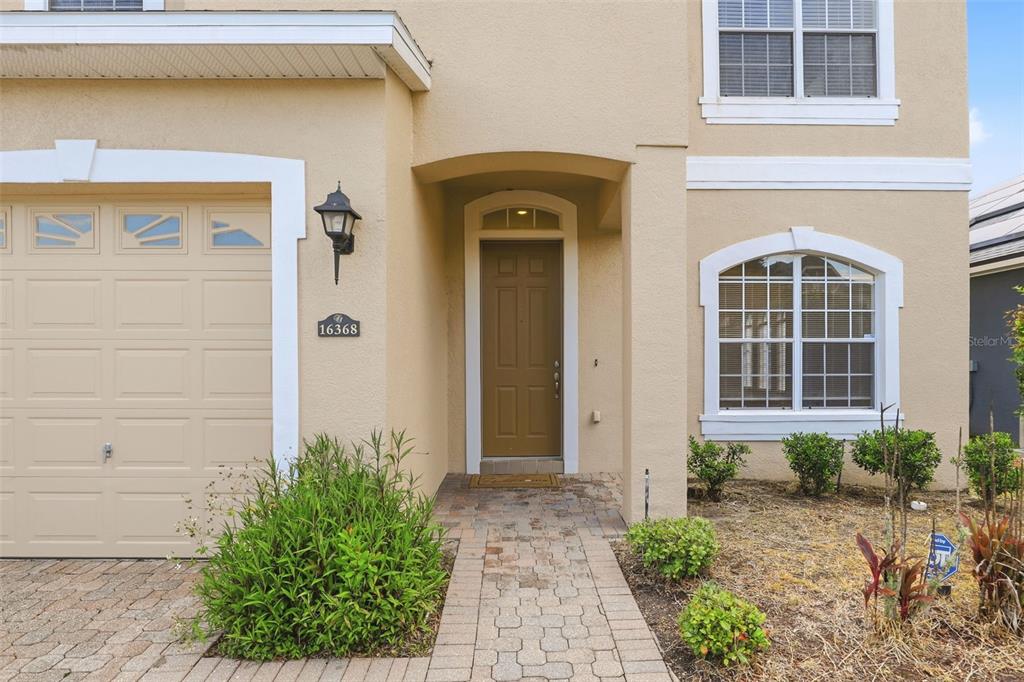 The exterior of a two-story tan house features a garage, a front door, and landscaping — 16368 TUDOR GROVE DRIVE, ORLANDO, FL