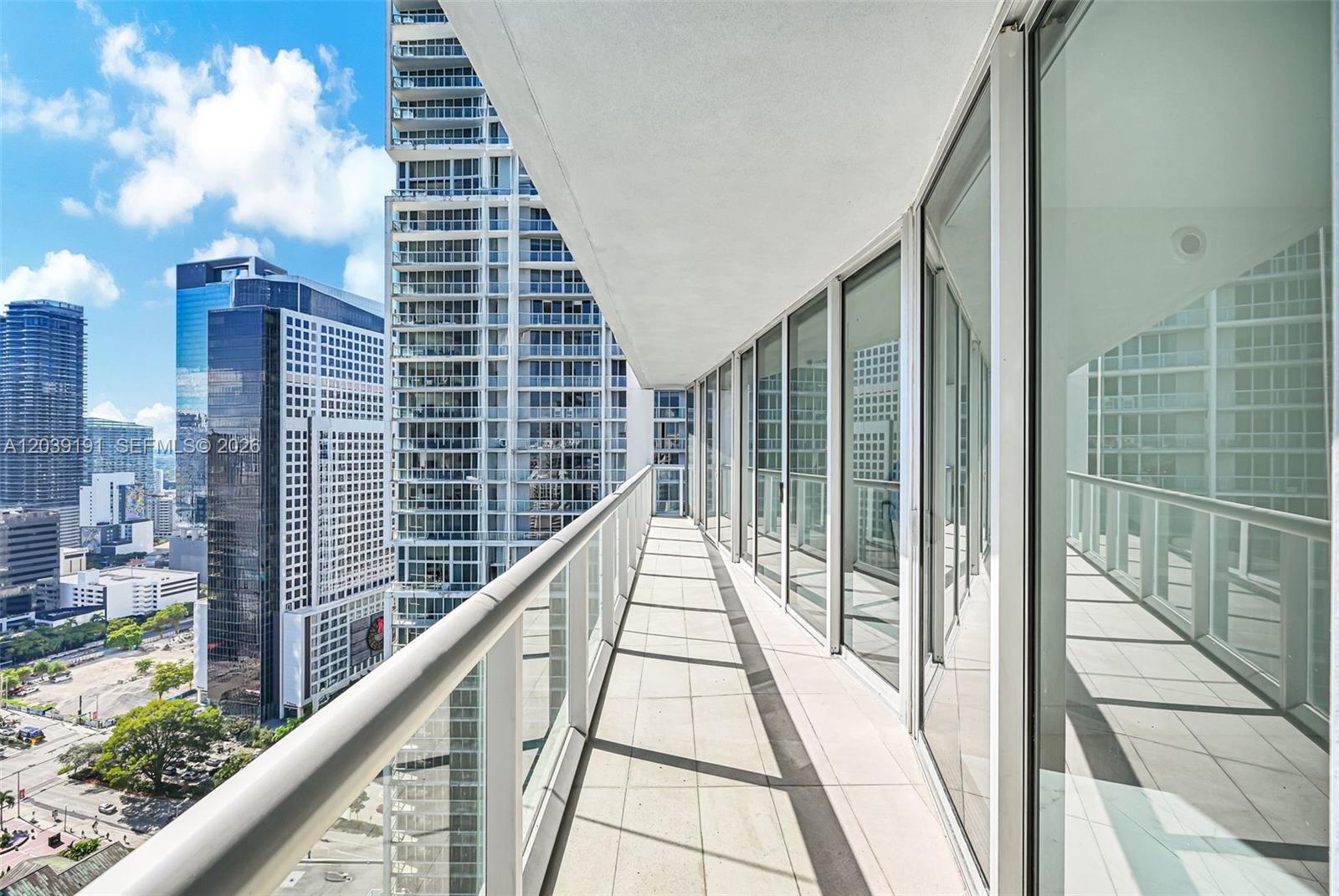 A high-rise balcony features a glass railing and floor-to-ceiling windows overlooking a city skyline — 475 Brickell Ave # 3113, Miami FL 33131, MIAMI, FL