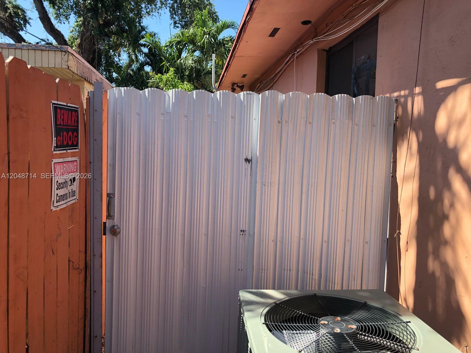 A white corrugated metal gate stands between a wooden fence and a peach-colored building wall — 2460 NW 15th St # 4, Miami FL 33125, MIAMI, FL